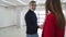 Adult gray-haired man in glasses and sweater approaches woman and shakes hands while talking, view from woman\'s back
