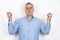 Adult handsome man with grey hair wearing blue shirt standing in peaceful yoga position on isolated white background