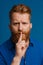 Adult handsome redhead bearded frowning man doing silence gesture