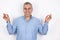 Adult happy man with grey hair wearing blue shirt standing in peaceful yoga position on isolated white background, body