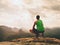 Adult hiker in black shorts and green singlet sit on mountain edge. Man enjoying view