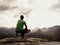 Adult hiker in black shorts and green singlet sit on mountain edge. Man enjoying view