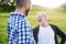 An adult hipster son with senior father on a walk in nature at sunset.