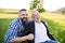 An adult hipster son with senior father in wheelchair on a walk in nature at sunset, laughing.