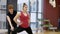 Adult instructor helps a woman with stretch of leg muscles standing in gym.
