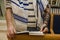 An adult jewish man praying with a tefillin on his arm, holding a bible book, while reading a pray