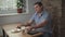 Adult male in a blue shirt in the morning sitting in a cafe drinking coffee and eating toast, is on the table and tablet