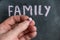 Adult male holding a piece of colored chalk in his hand. Handwritten word FAMILY on black chalkboard