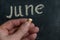 Adult male holding a piece of yellow chalk in his hand. Handwritten word JUNE on black chalkboard. Selective focus