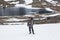 Adult man backpacker standing on snow patch while hiking in mountains, mountaineering with backpack, mountain lake landscape with