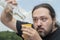 An adult man with a beard is trying to pour wine from a nearly empty bottle into a plastic cup