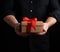 Adult man in a black shirt holds in his hand a square brown boxlet tied with a red ribbon on a black background