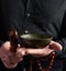 Adult man in a black shirt rotates a wooden stick around a copper Tibetan bowl of water. ritual of meditation