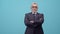 Adult man businessman in glasses and a jacket folds arms with a cross on chest and looks into camera in the studio on