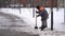 Adult man cleaning path from snow in winter season. Worker removes snow with shovel on walkway in park.