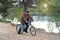 An adult man in a corduroy brown jacket rides a bicycle in a park