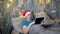 An adult man in a red Santa Claus hat flips through web pages on a tablet while lying on a bed in the bedroom at night
