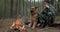 Adult Man is relaxing at the fire with his dog in the nature. Alone traveler is resting with his German shepherd by the forest