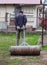 Adult man rolling heavy iron barrel for better condition garden after winter. Human wears working outfit. Manual work in the