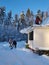 An adult man shovels snow from the roof of the veranda of a country house, a young man removes snow downstairs, a girl looks