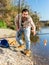 Adult man standing near river and pulling fish expressing emotions of dedication