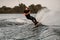 Adult man in wetsuit holds cable in his hands and wakeboarding on splashing wave