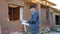 Adult man working on site of modern house and standing outdoors with paper draft looking away