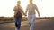 Adult mature couple walking holding hands with love and romance on a street with sunset in backlight and background - forever toge