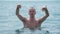 Adult middle-aged man in the sea. Cheerful man raises two hands above water
