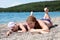 Adult mother with her young daughter sunbathing on the beach, laying on sand. Looking at a camera