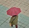 An adult person standing and holding a red, black checkered umbrella during a rainy day