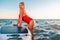 An adult plump woman in a red swimsuit posing in the sea with a sap board. Copy space. The concept of active recreation