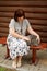 An adult plump woman sits on a bench near a log house and strokes a gray cat