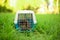 The adult rabbit is sitting in closed travel pet carrier in the grass in outdoors