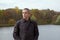 Adult retired man stands by the lake on beautiful autumn day