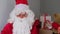 Adult santa claus in red suit sits at table, Christmas tree is beautifully decorated with balls, garlands, concept of christmas,