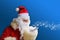 Adult santa claus with white beard on a beautiful blue background blows snow from the palm, christmas concept, waiting for gifts,