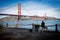 Adult standing on a pier surrounded by dogs against a backdrop of the iconic Golden Gate Bridge