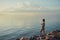 Adult standing on rocks with teacup and watching setting sun