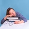 Adult tired woman sleeping on books while studying, blue background