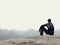 Adult tourist in black trousers, jacket and dark cap sit on cliff`s edge and looking into mist