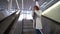 Adult townswoman is talking by phone standing on moving staircase in airport or railway station