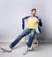 Adult unshaved man in torn jeans, yellow t-shirt sits on stool with his blue jacket open, showing that he had nothing