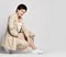 Adult woman in beige business casual pantsuit and sneakers sits squatted and sideways. Stylish business female wear
