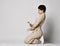 Adult woman in beige business casual pantsuit and sneakers stands on knees holding belt. Stylish business female wear