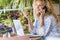 Adult woman calling at the phone sitting on the table. Pretty female people speaking and using mobile cellular and laptop at the