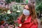 An adult woman in a face mask looks at white potted roses grown in the greenhouse of a flower shop