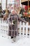 an adult woman in a fur coat on a festive square with a bouquet of Christmas trees.