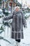 an adult woman in a fur coat on a festive square with a bouquet of Christmas trees.