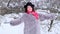 An adult woman in a fur coat and a hat throws snow in front of her, spins and gives an air kiss in winter in a park in slow motion